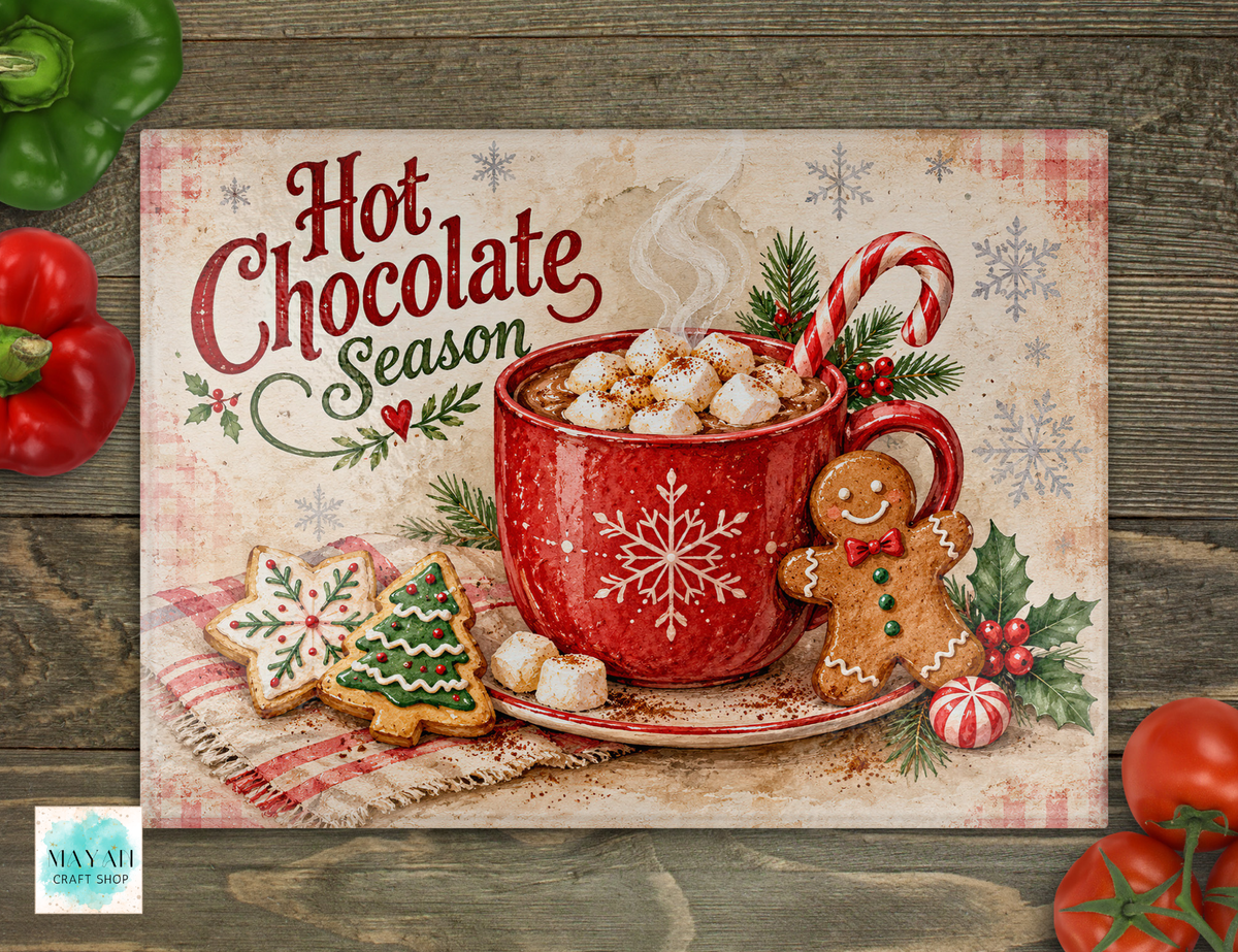 A cutting board featuring a festive Christmas hot chocolate scene, with the words 'Hot Chocolate Season' in red script. The design shows a red mug filled with marshmallows and cocoa, candy canes, snowflakes, gingerbread cookies, and holly, placed on a rustic wood surface with red bell peppers around it.