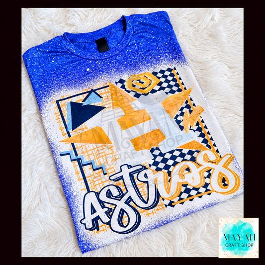 A blue and white gradient t-shirt with a colorful baseball graphic design, laid flat on a white faux fur background. The design features orange, yellow, and navy blue geometric shapes.