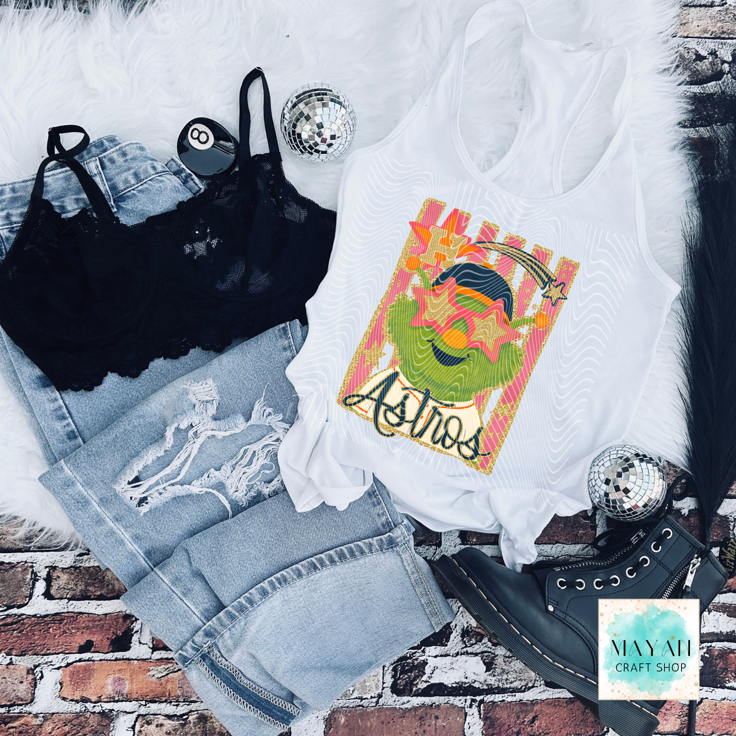 White tank top with vibrant graphic, black bralette, denim shorts, and black high-heeled shoes on a brick surface.