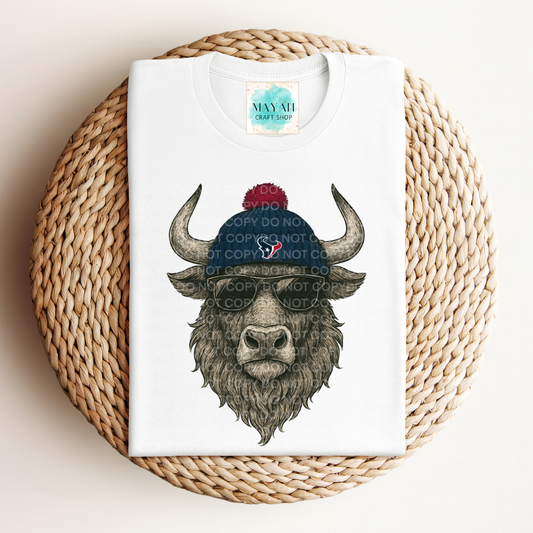 White t-shirt with a graphic of a bison wearing a blue beanie with a red logo, placed on a woven mat.