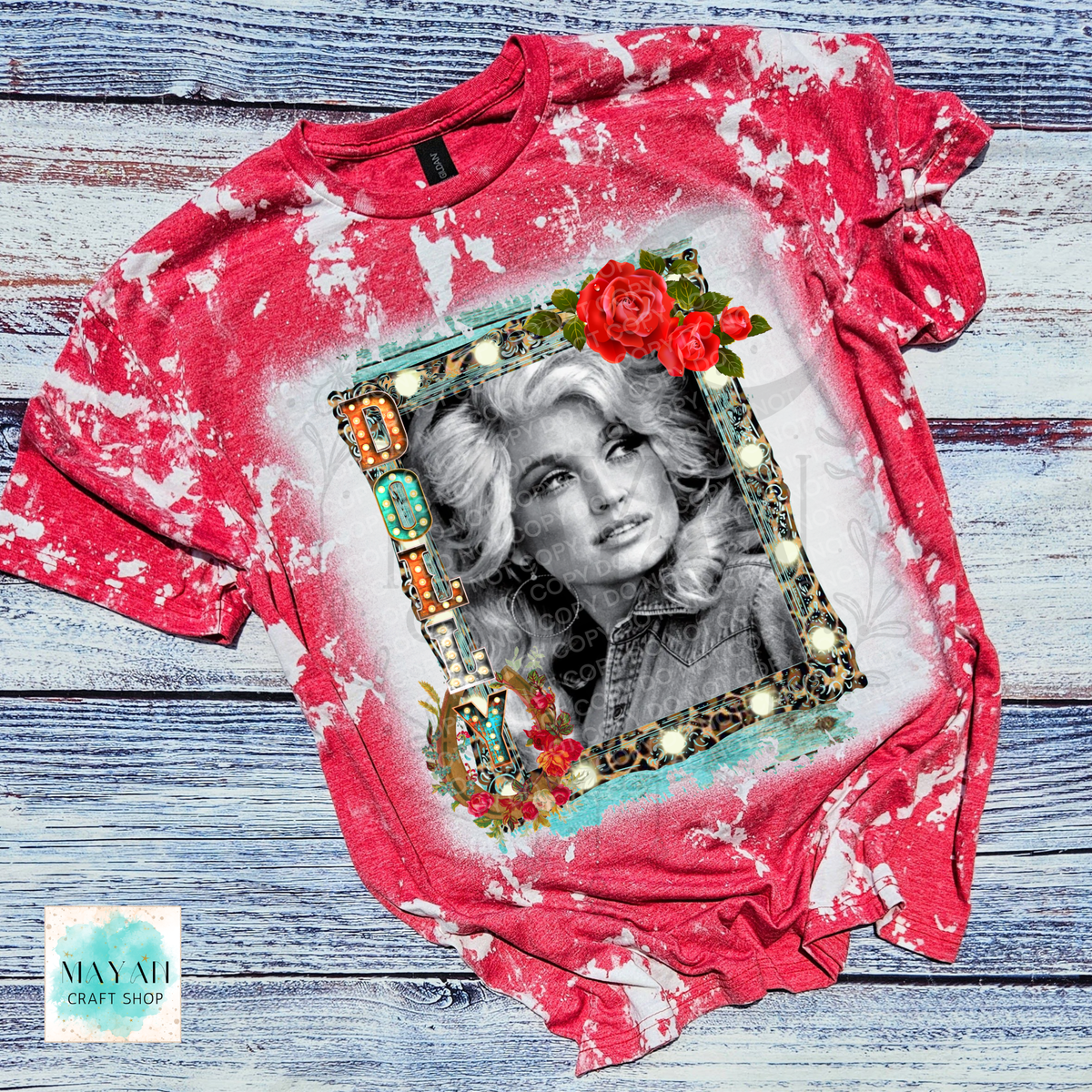 A red and white tie-dye graphic t-shirt laid flat on a rustic blue-gray wooden background. The shirt features a central black-and-white portrait of a woman framed by red roses and gold accents.