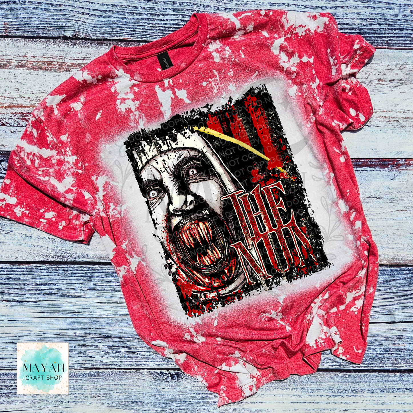 A red bleached graphic t-shirt featuring a horror design of a screaming face with a text on the front, laid flat on a rustic blue-gray wooden background.