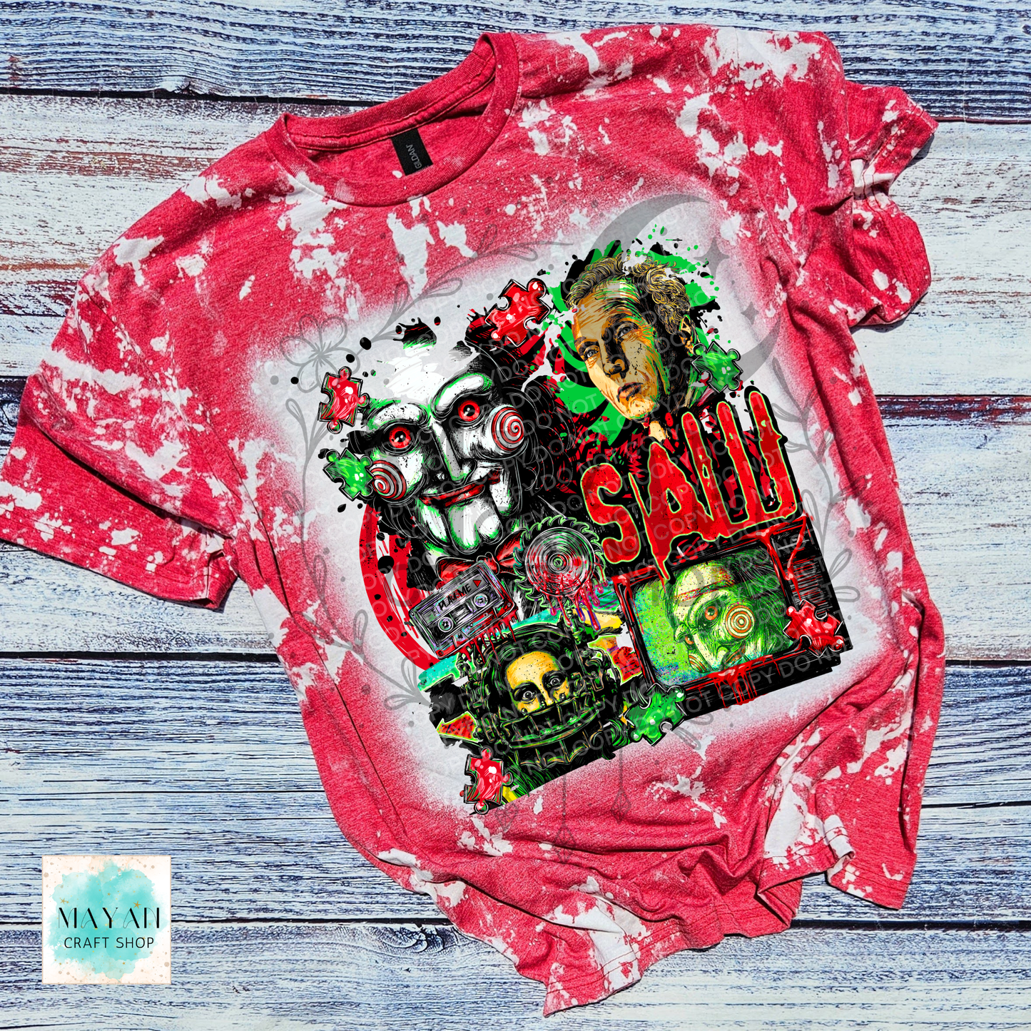 A red bleached graphic t-shirt featuring a horror collage of horror character and skulls. The shirt is laid flat on a rustic, weathered blue-gray wooden plank background.