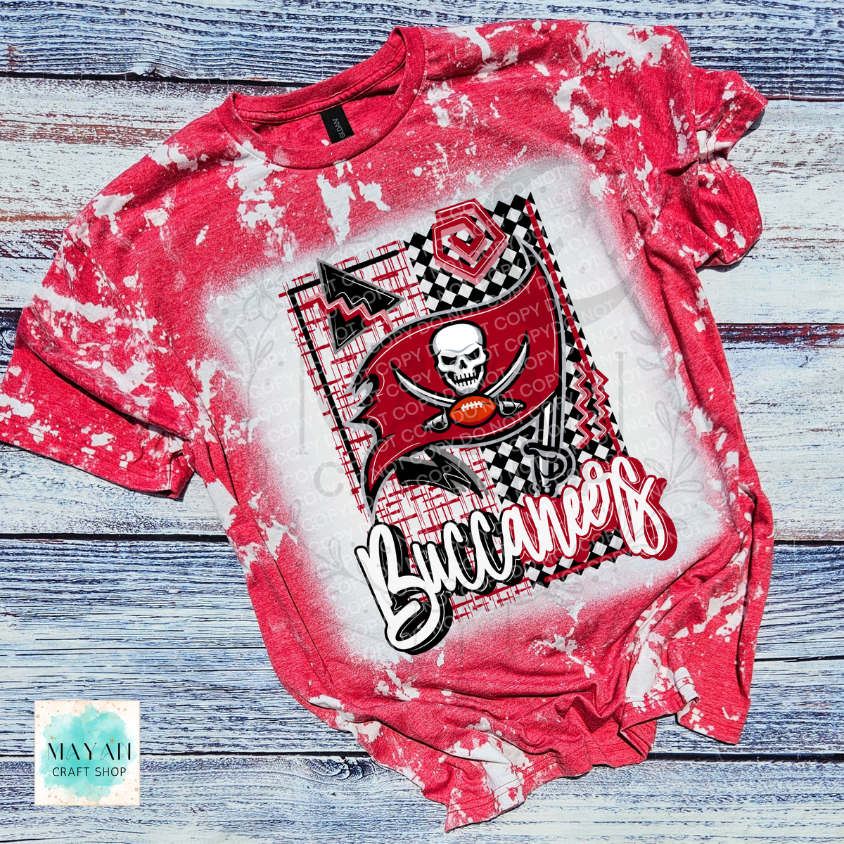 A heather red bleached t-shirt featuring a pirate design with a skull, crossed cutlasses, a football, with a pirate flag and football, laid flat on a rustic blue-gray wood plank background.