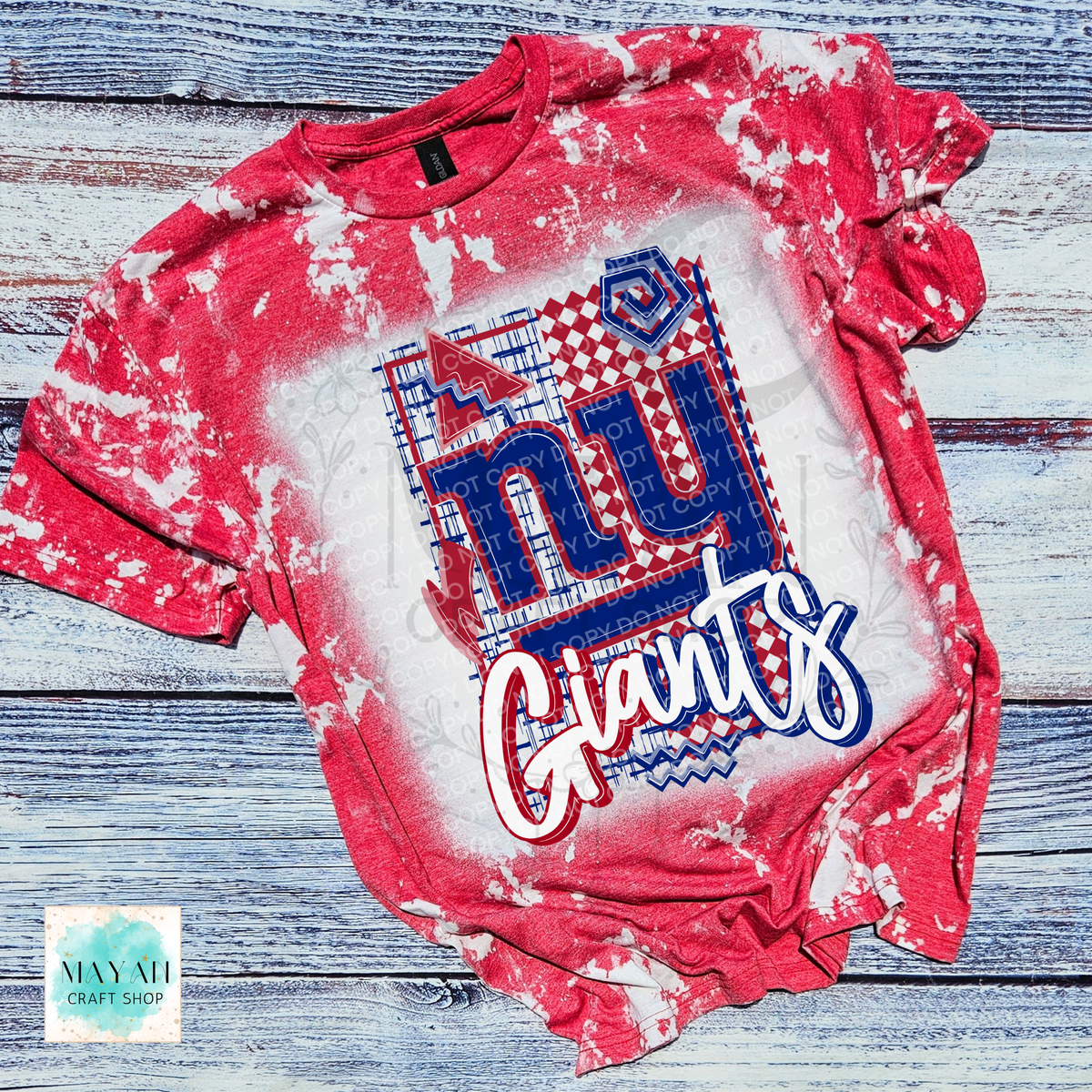 A heather red bleached t-shirt featuring a football team graphic print, laid flat on a rustic blue-gray wooden background. 