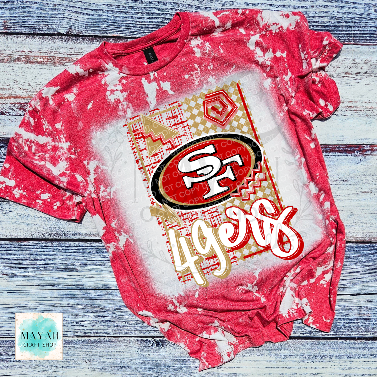 A heather red  short-sleeve t-shirt featuring a football team logo graphic print on the front, laid flat on a rustic blue-gray wood plank background.
