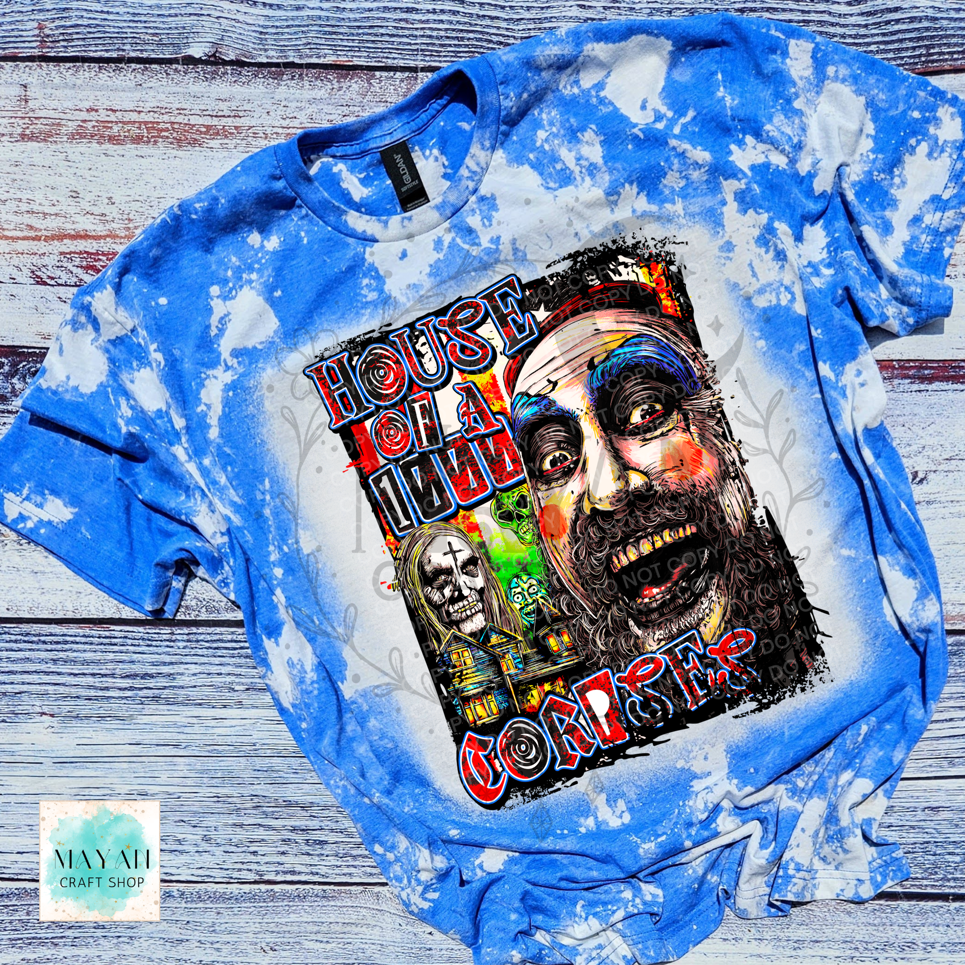 A blue bleached t-shirt featuring a large graphic print of a creepy face with a text in red and black. The t-shirt is laid flat on a rustic, weathered gray wood background.