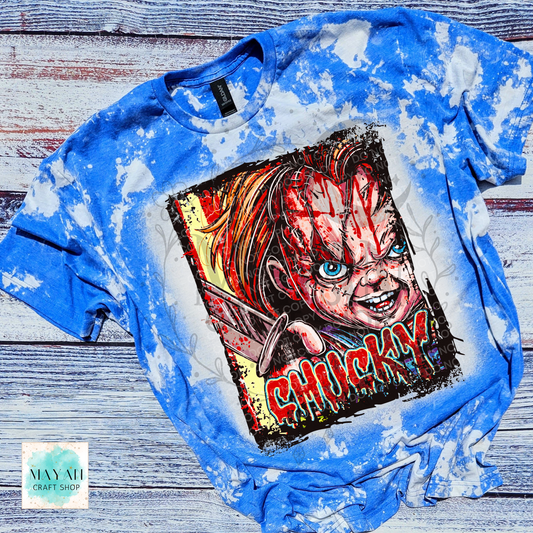 A blue bleached graphic t-shirt featuring a horror character print with a text in red. The t-shirt is laid flat on a rustic, weathered gray wood background.