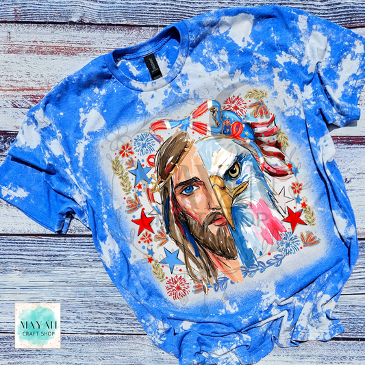 Blue tie-dye t-shirt with a graphic design of a man with an eagle head and American flag elements on a wooden surface.