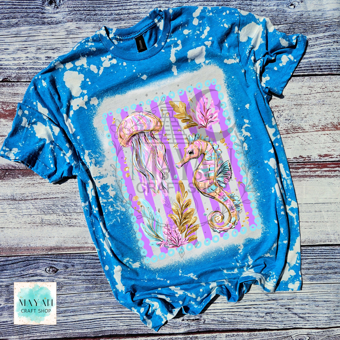Bleached blue t-shirt with a colorful seahorse and jellyfish design on a wooden surface.