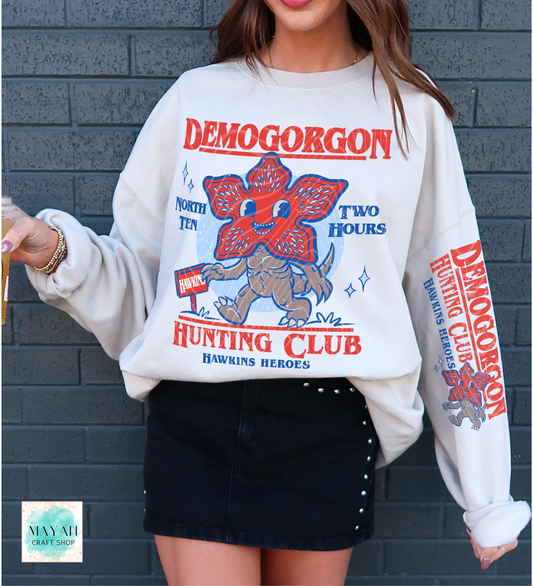 Person wearing a white sweatshirt with 'Hunting Club' design against a gray brick wall.
