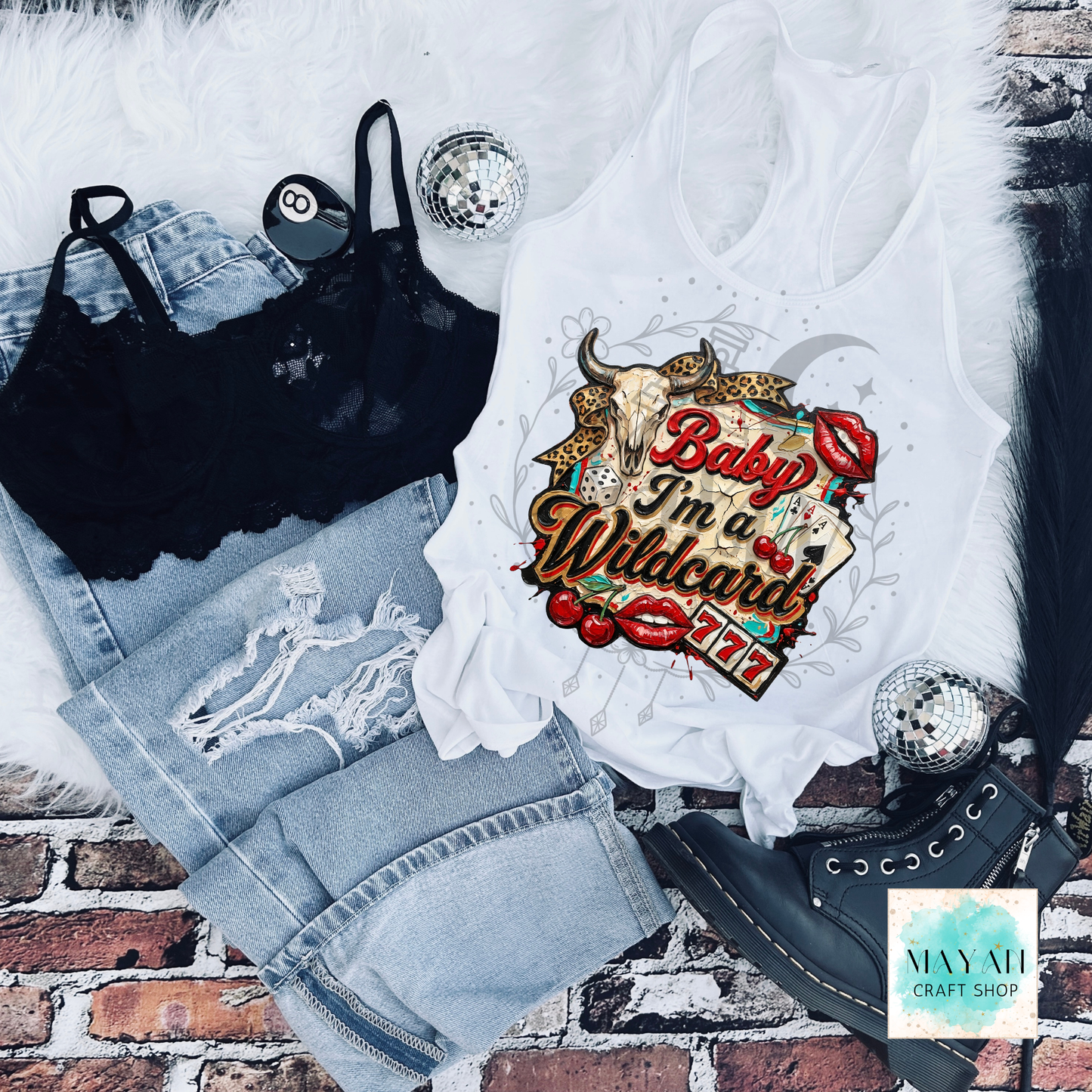 White tank top with graphic design, black bralette, denim shorts, and black high-heeled shoes on a brick surface.