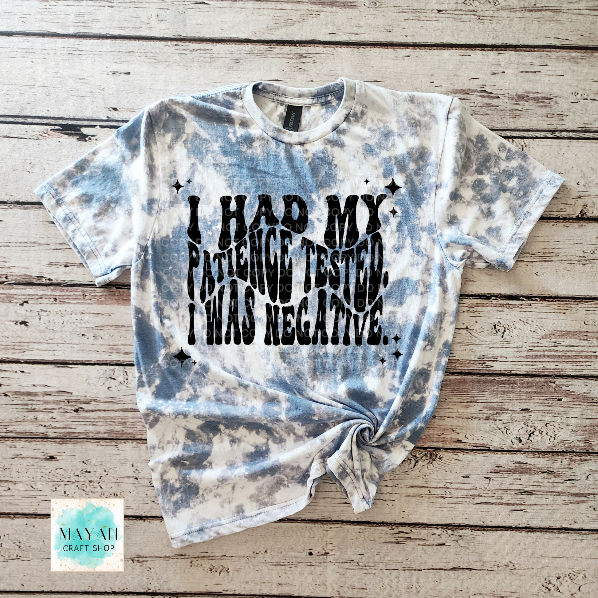 Tie-dye t-shirt with text on a wooden surface, featuring the brand 'Mayan Craft Shop'.