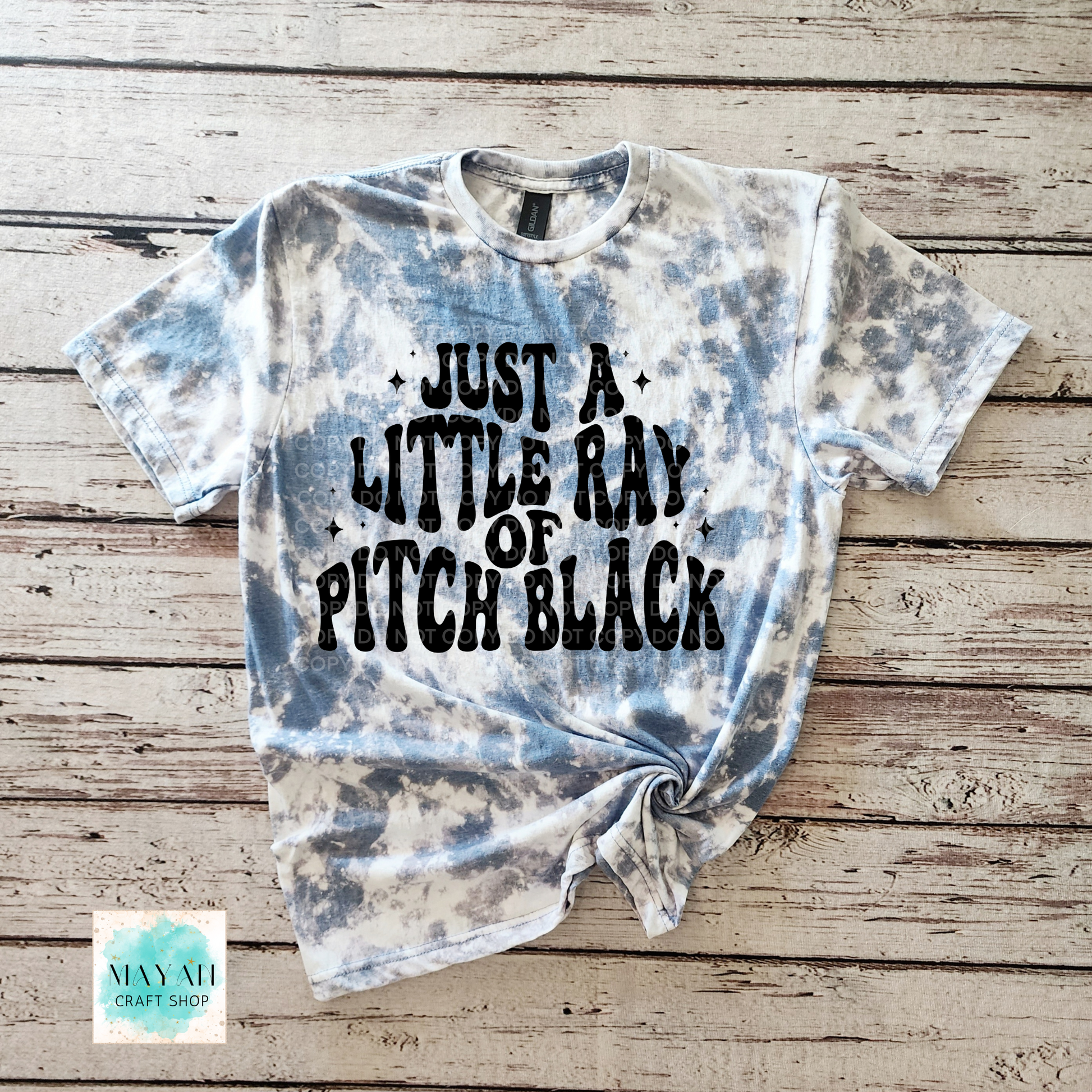 Tie-dye t-shirt with text on a wooden surface, featuring the brand 'Mayan Craft Shop'.
