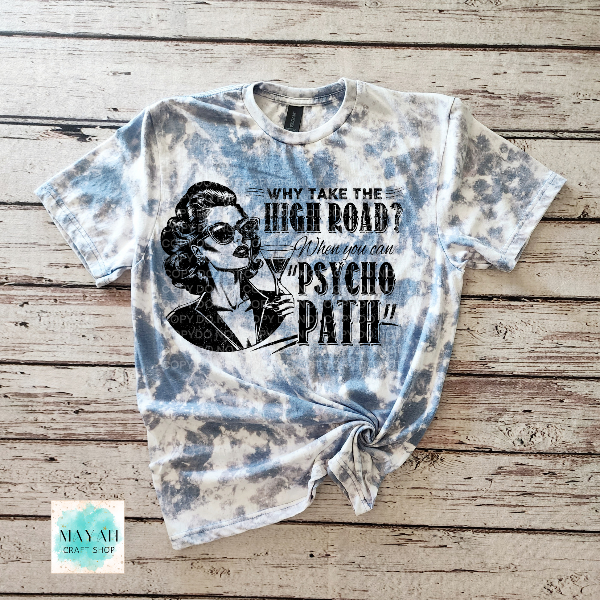 Tie-dye t-shirt with graphic design and text on a wooden surface, featuring the brand 'Mayan Craft Shop'.