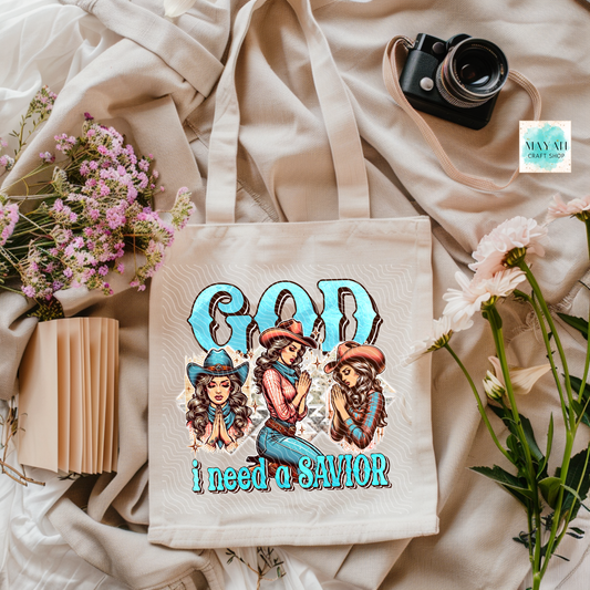 Tote bag with graphic design featuring three women in cowboy hats and text 'God I need a SAVIOR' on a soft fabric background.