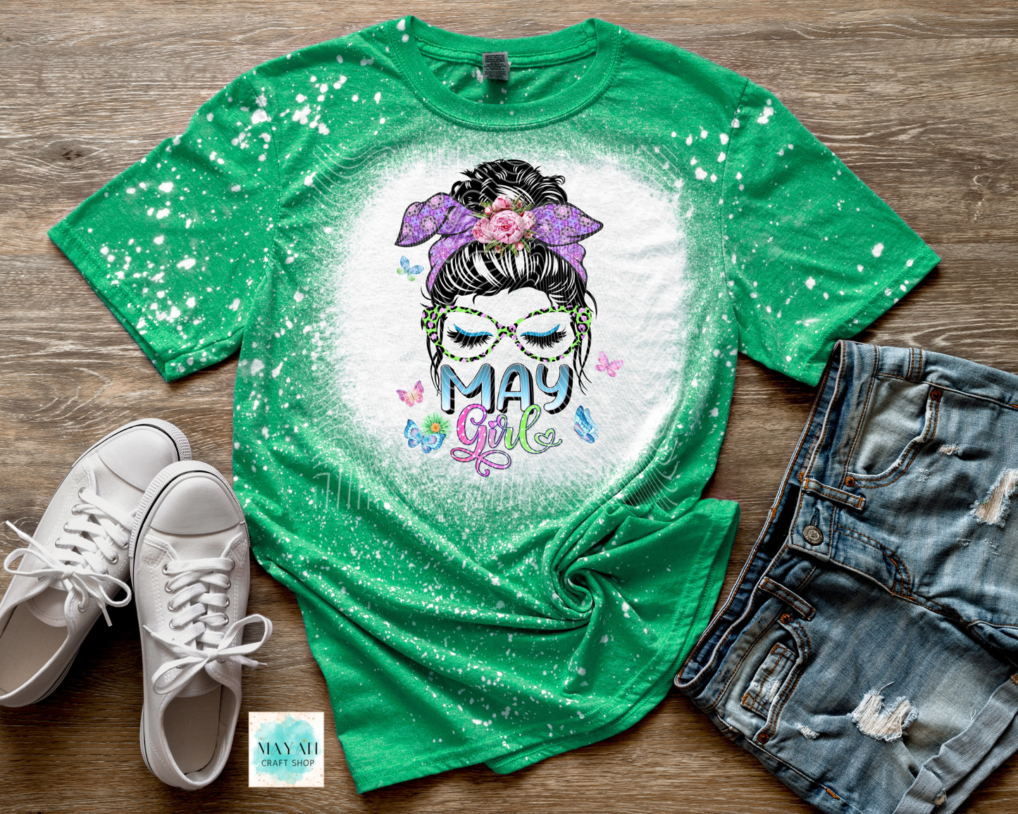Green t-shirt with 'May Girl' design on a wooden surface with white sneakers and denim shorts.