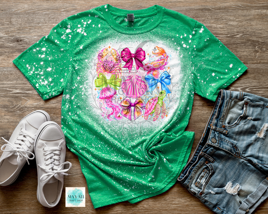 Green t-shirt with colorful graphic design on a wooden surface with white sneakers and denim shorts.