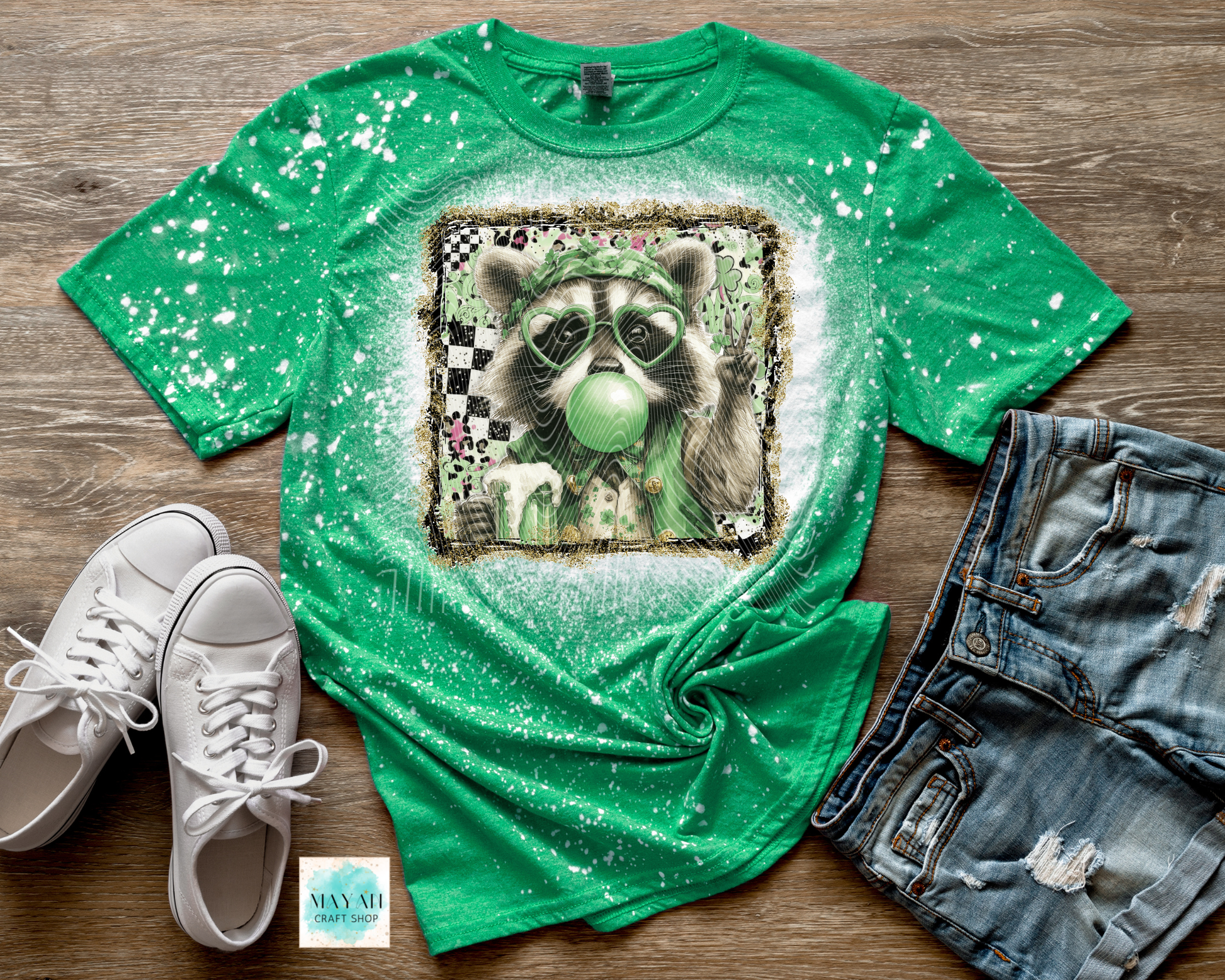 Green t-shirt with raccoon graphic, white sneakers, and denim shorts on a wooden surface