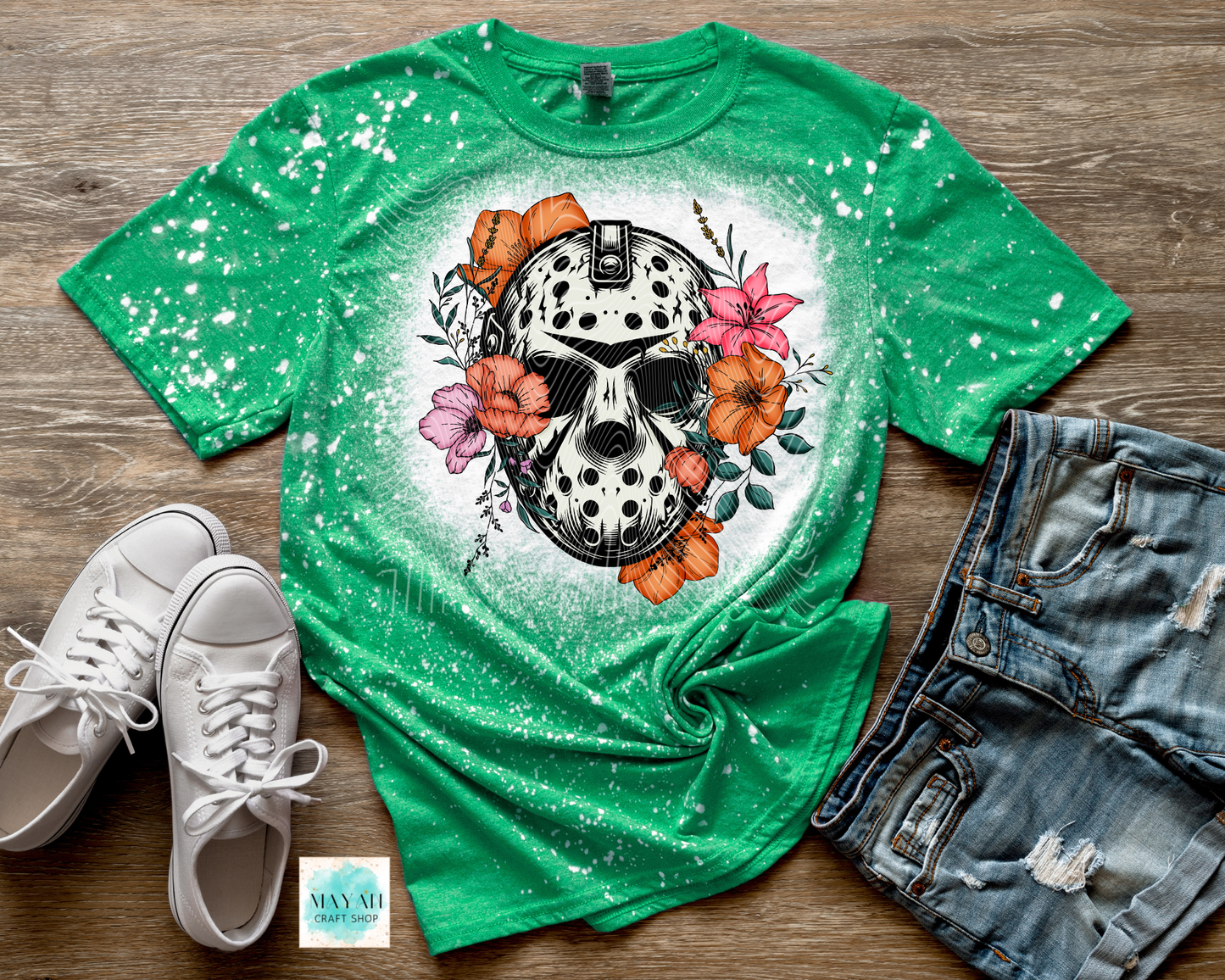 Green t-shirt with skull and floral design on a wooden surface with sneakers and jeans.