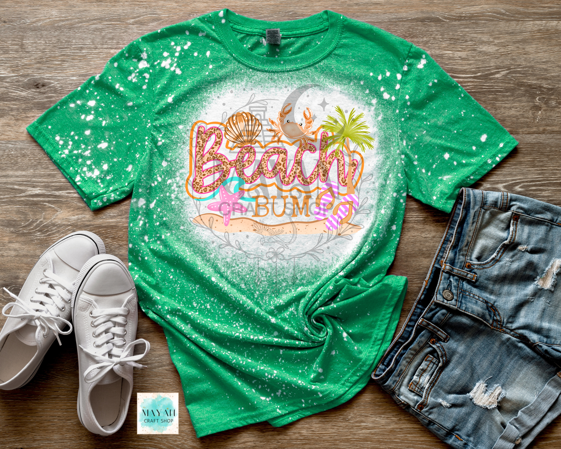 Green t-shirt with 'Beach Bum' design on a wooden surface with white sneakers and denim shorts.