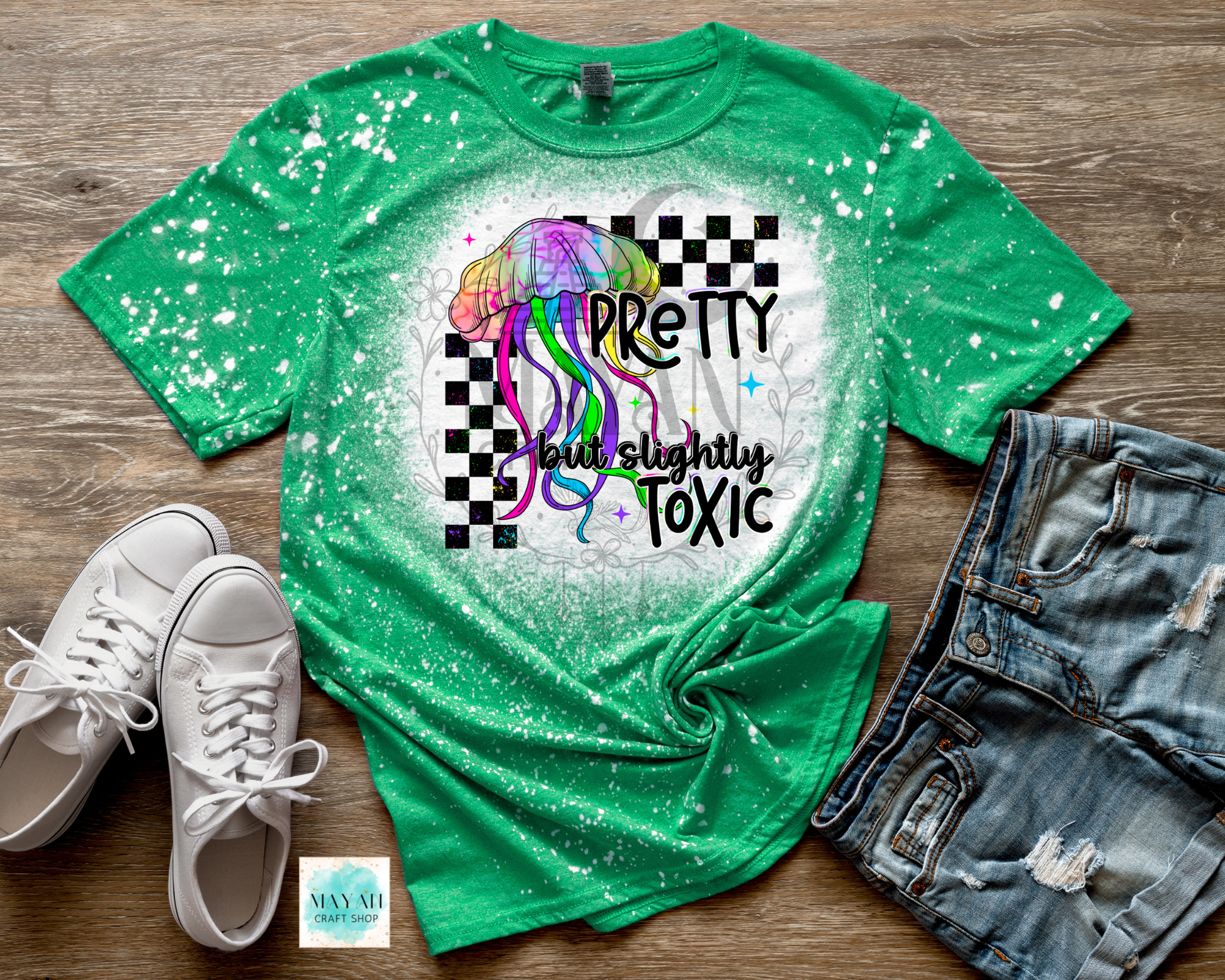 Green t-shirt with colorful design and text on a wooden surface with shoes and jeans.