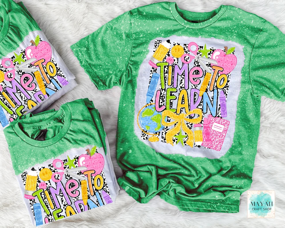 Three green short-sleeve t-shirts with a white tie-dye effect and a colorful 'Time To Learn' school-themed graphic, arranged on a white faux fur background.