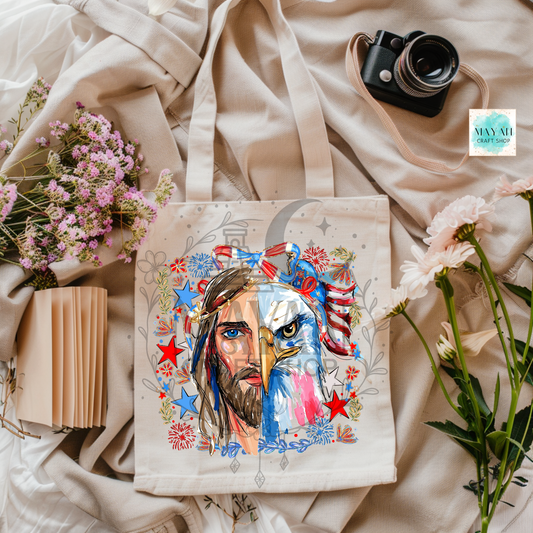 Canvas tote bag with artistic design of a face and eagle, surrounded by flowers and a camera on a soft fabric background.