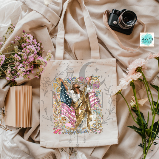 Tote bag with artistic design of a person holding an American flag, surrounded by flowers and a camera on a soft fabric background.