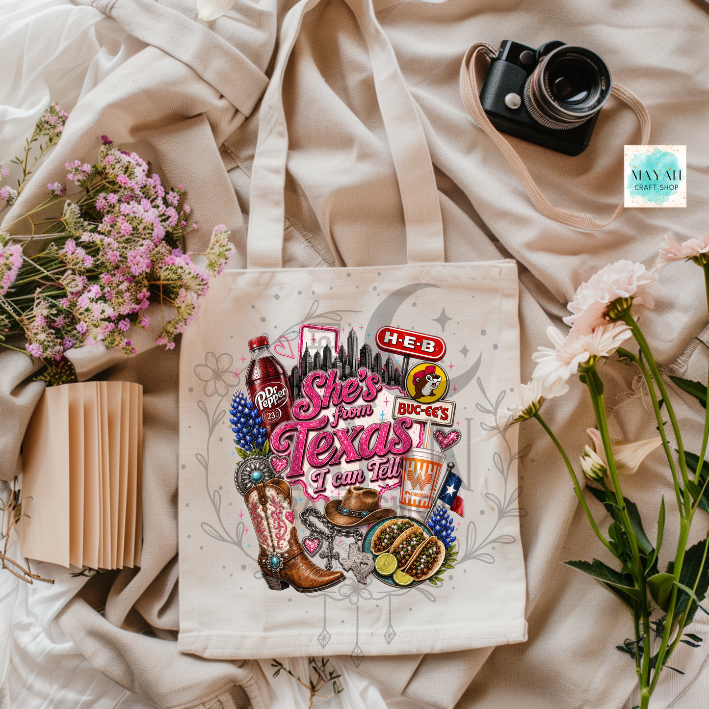 Tote bag with Texas-themed graphics on a light fabric background with flowers and a camera.