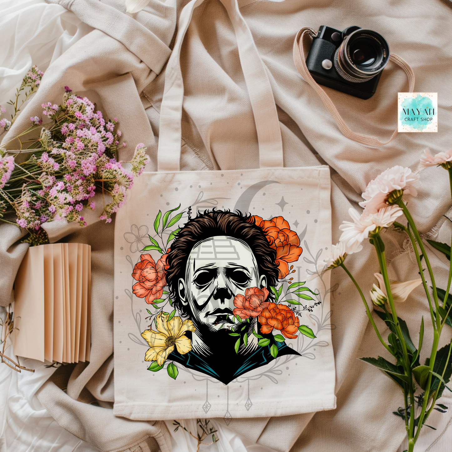 Tote bag with a design of a face surrounded by flowers on a soft fabric background.