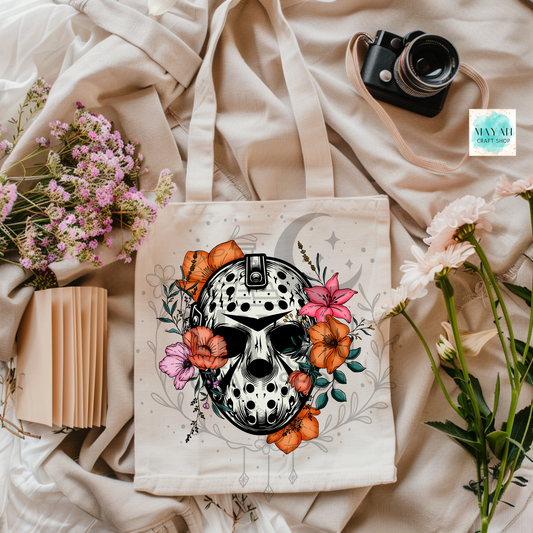 Tote bag with a mask and floral design on a beige fabric background with flowers and a camera.