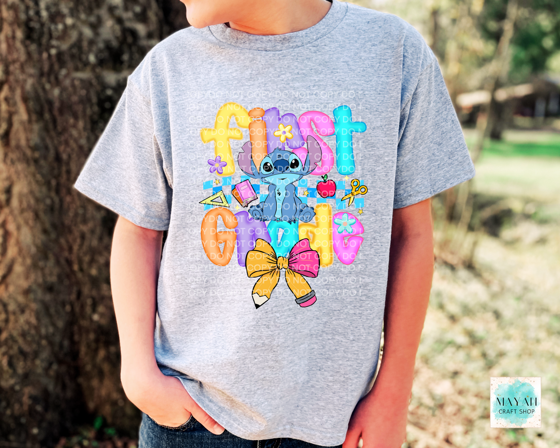 Child wearing a gray t-shirt with colorful graphics and text, standing outdoors.