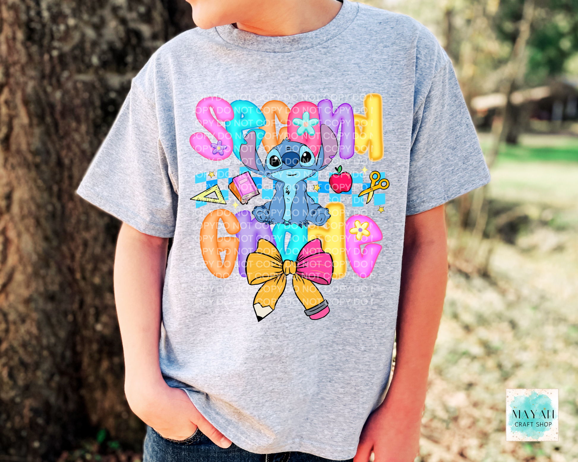 Child wearing a gray t-shirt with colorful graphics and text, standing outdoors.