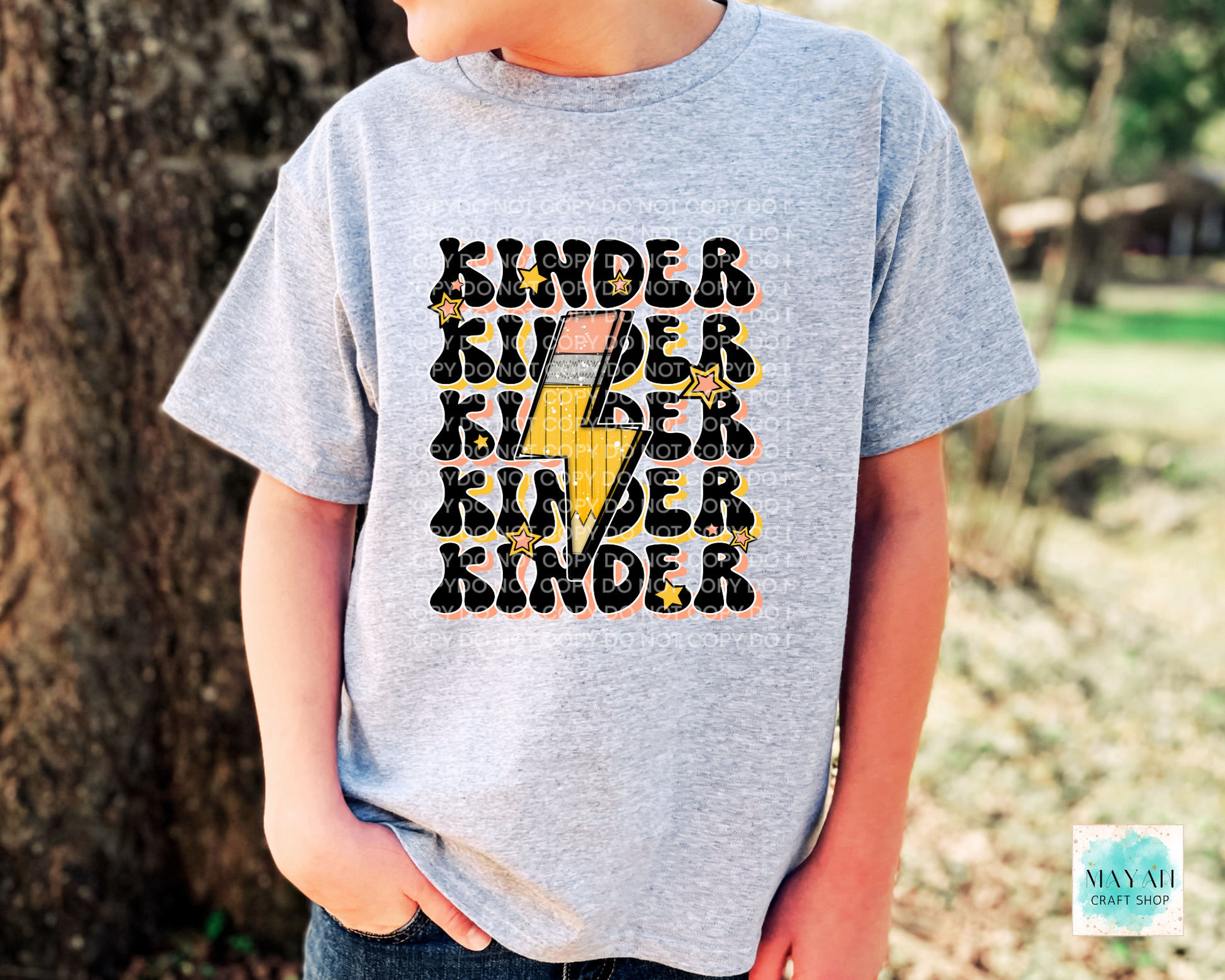 Child wearing a gray t-shirt with 'Kinder' text design outdoors.