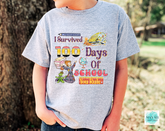 Child wearing a t-shirt with 'I survived 100 days of school' text and graphics outdoors.
