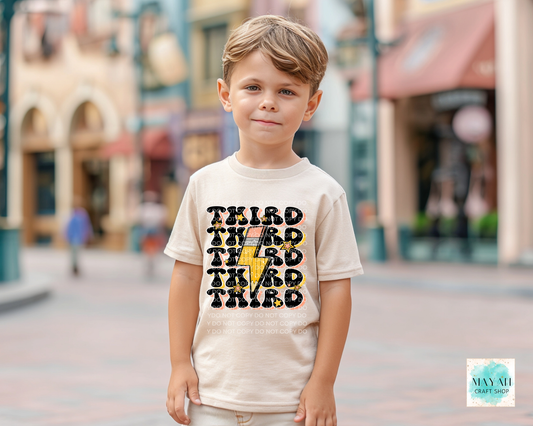 Child wearing a t-shirt with 'THIRD' printed on it, standing in an outdoor setting.