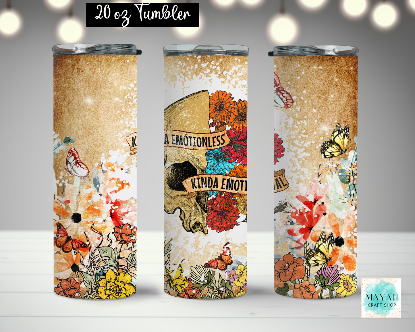 Three views of a 20 oz tumbler with a vintage-style graphic wrap. The design features a textured tan background with colorful illustrations of flowers, butterflies, and a skull with the text 'KINDA EMOTIONLESS'.