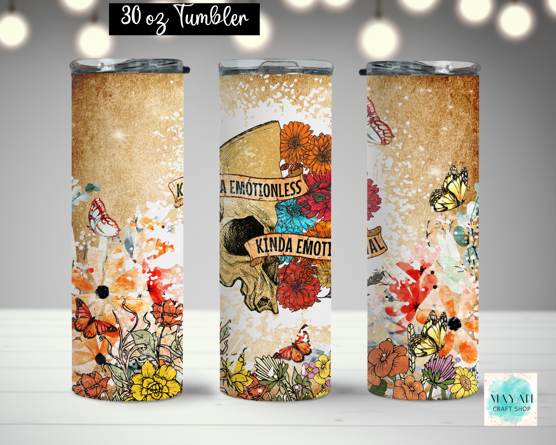 Three views of a 30 oz tumbler with a vintage-style graphic wrap. The design features a textured tan background with colorful illustrations of flowers, butterflies, and a skull with the text 'KINDA EMOTIONLESS'.