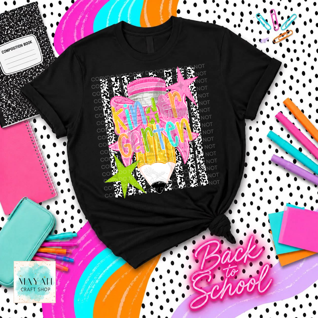 A black graphic t-shirt with a colorful 'Back to School' design featuring a pink and yellow paintbrush, starfish, and the words 'KINDERGARTEN' in pink letters. The shirt is styled in a flat-lay arrangement with school supplies and colorful curved stripes on a white polka dot background.