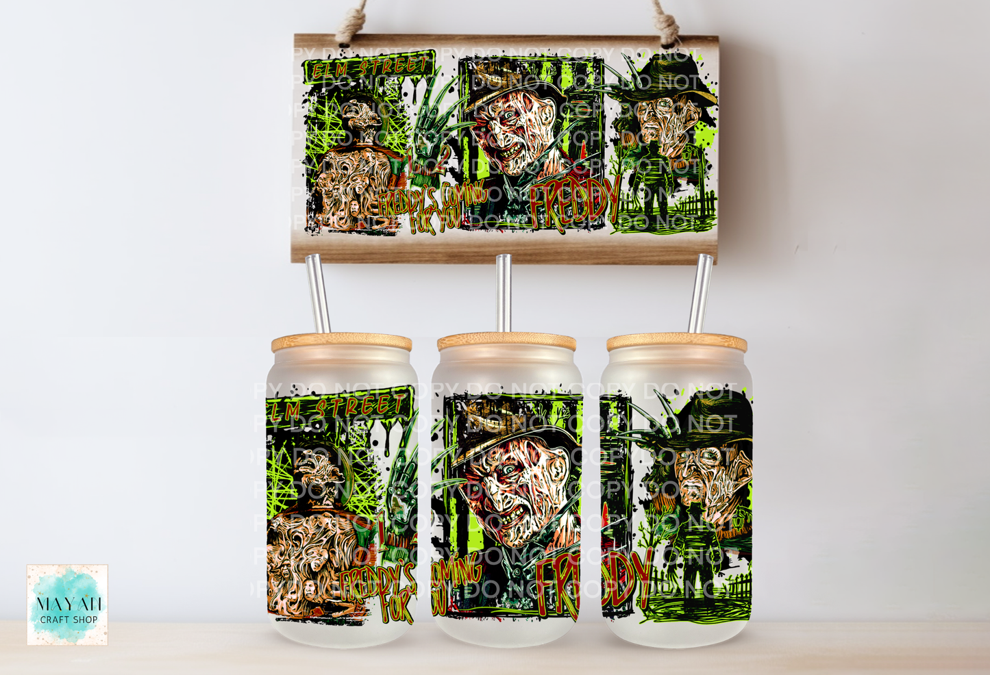 Three clear glass mason jar tumblers with light wood lids and metal straws, displayed below a matching rectangular sign. The tumblers and sign feature a dark collage-style graphic with green foliage and faces.