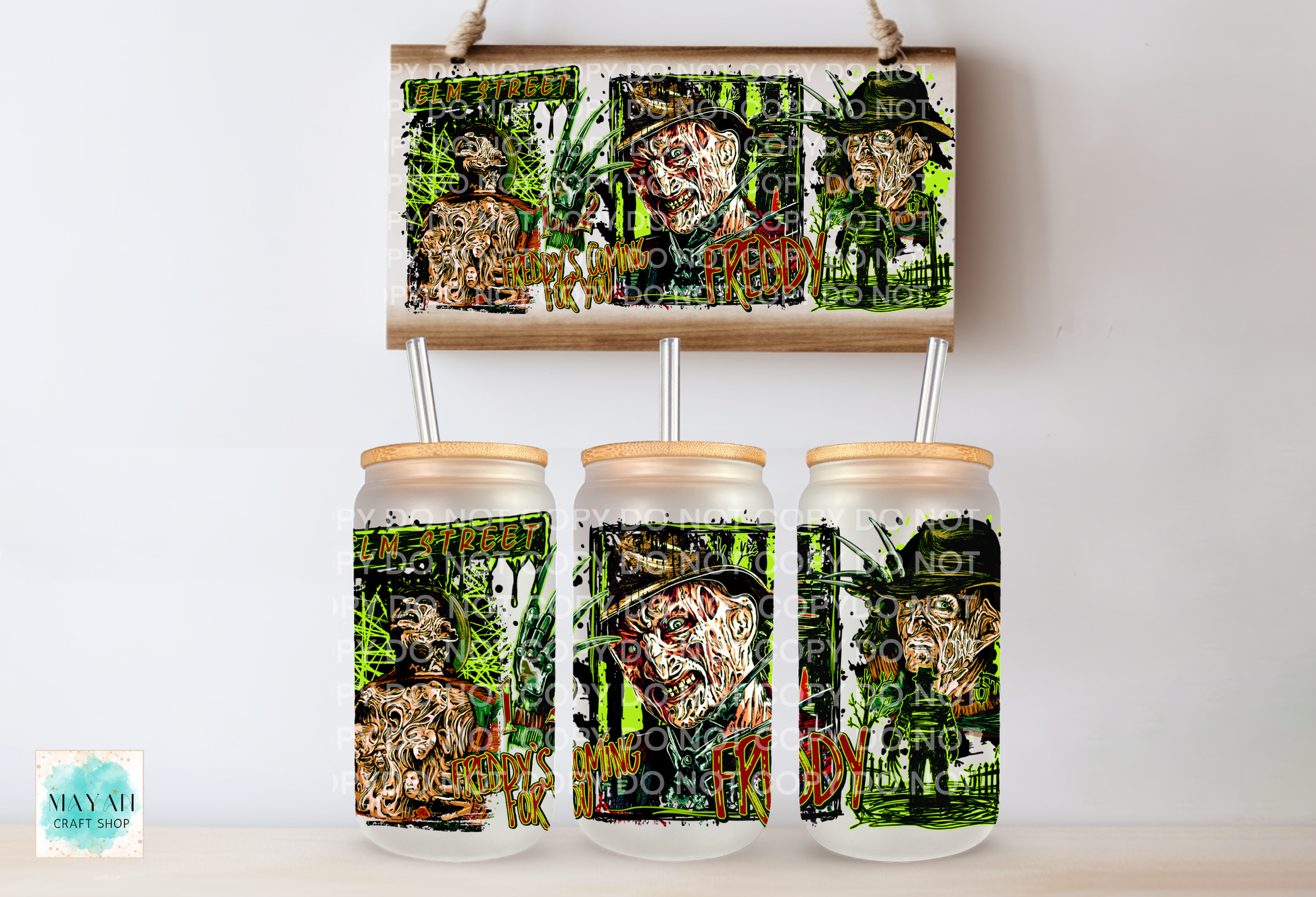 Three clear glass mason jar tumblers with light wood lids and metal straws, displayed below a matching rectangular sign. The tumblers and sign feature a dark collage-style graphic with green foliage and faces.