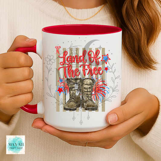Person holding a mug with 'Land of the Free' design featuring boots and stars.