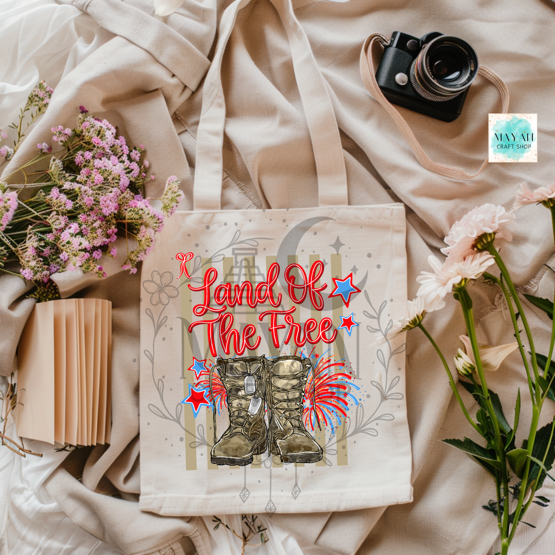 Tote bag with 'Land of the Free' text and boots design on a fabric background with flowers and a camera.