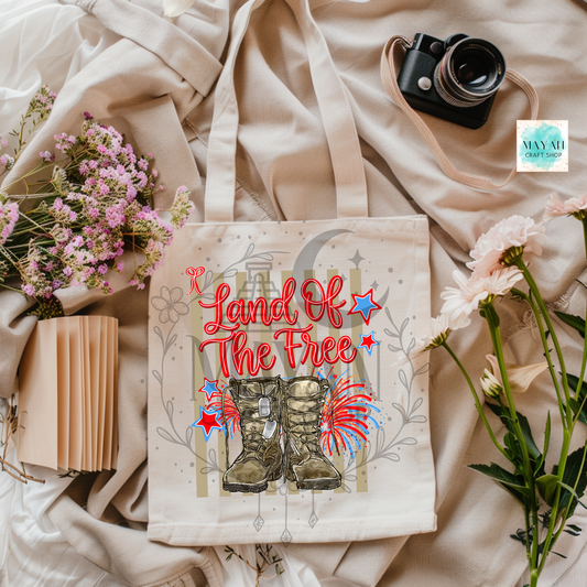 Tote bag with 'Land of the Free' text and boots design on a fabric background with flowers and a camera.
