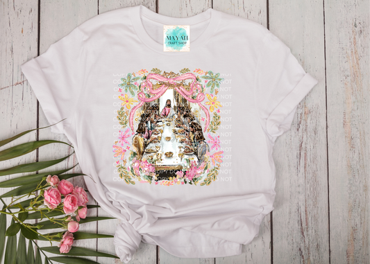White t-shirt with a colorful graphic design on a wooden surface with pink flowers and green leaves.