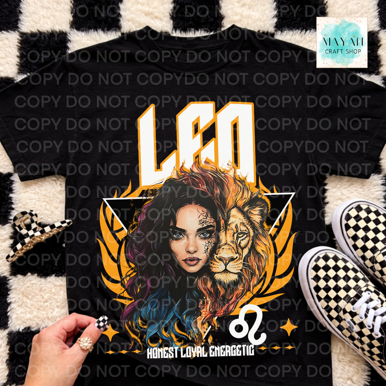 A black graphic t-shirt featuring a split lion and woman design with the text 'LEO' and 'HONEST LOYAL ENERGETIC', styled flat-lay on a black and white checkered rug with sneakers and a hand visible.