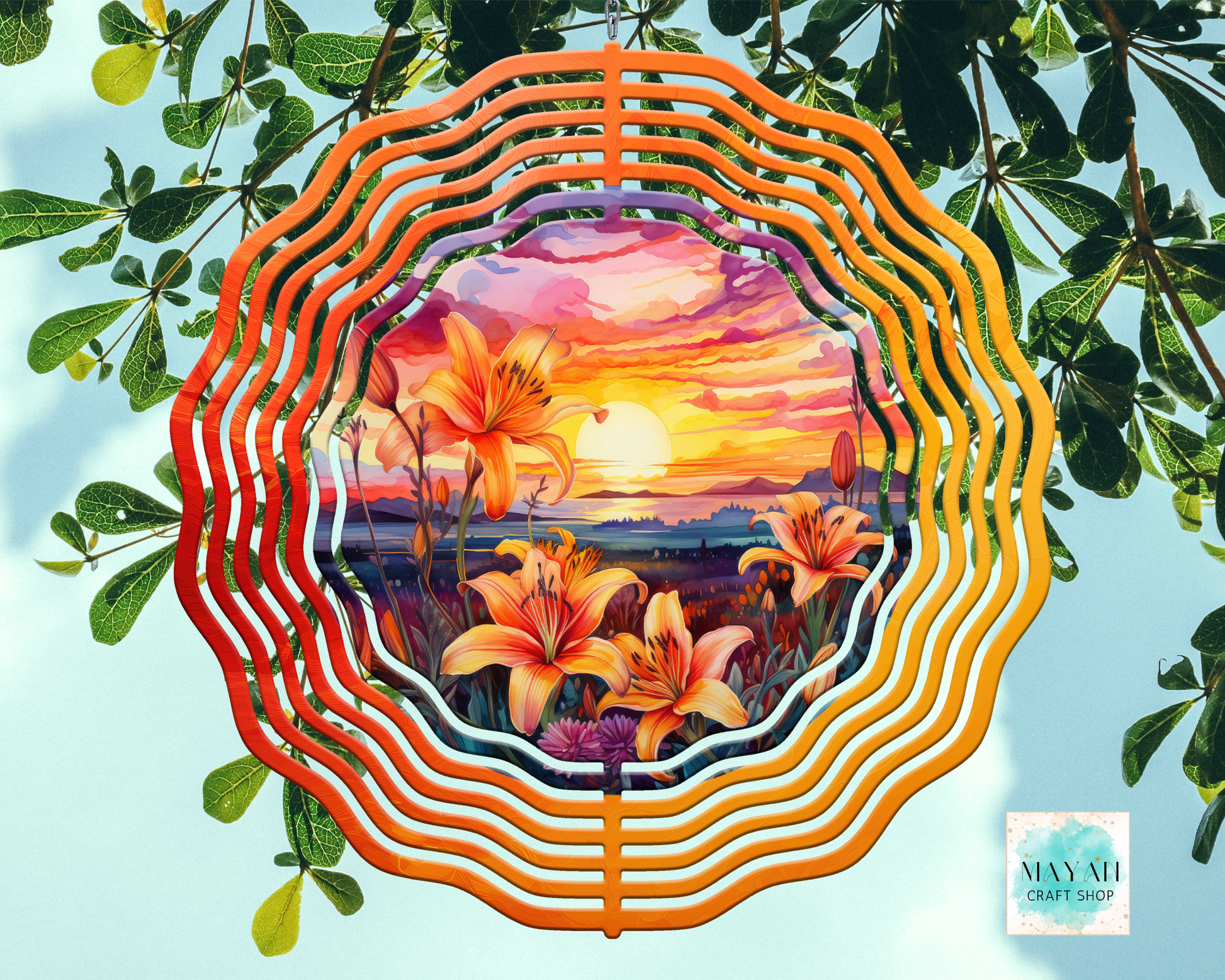 Decorative wind spinner with floral design and sunset scene, surrounded by green leaves.