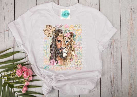 White t-shirt with a graphic of a man with a lion head and floral elements on a wooden surface.