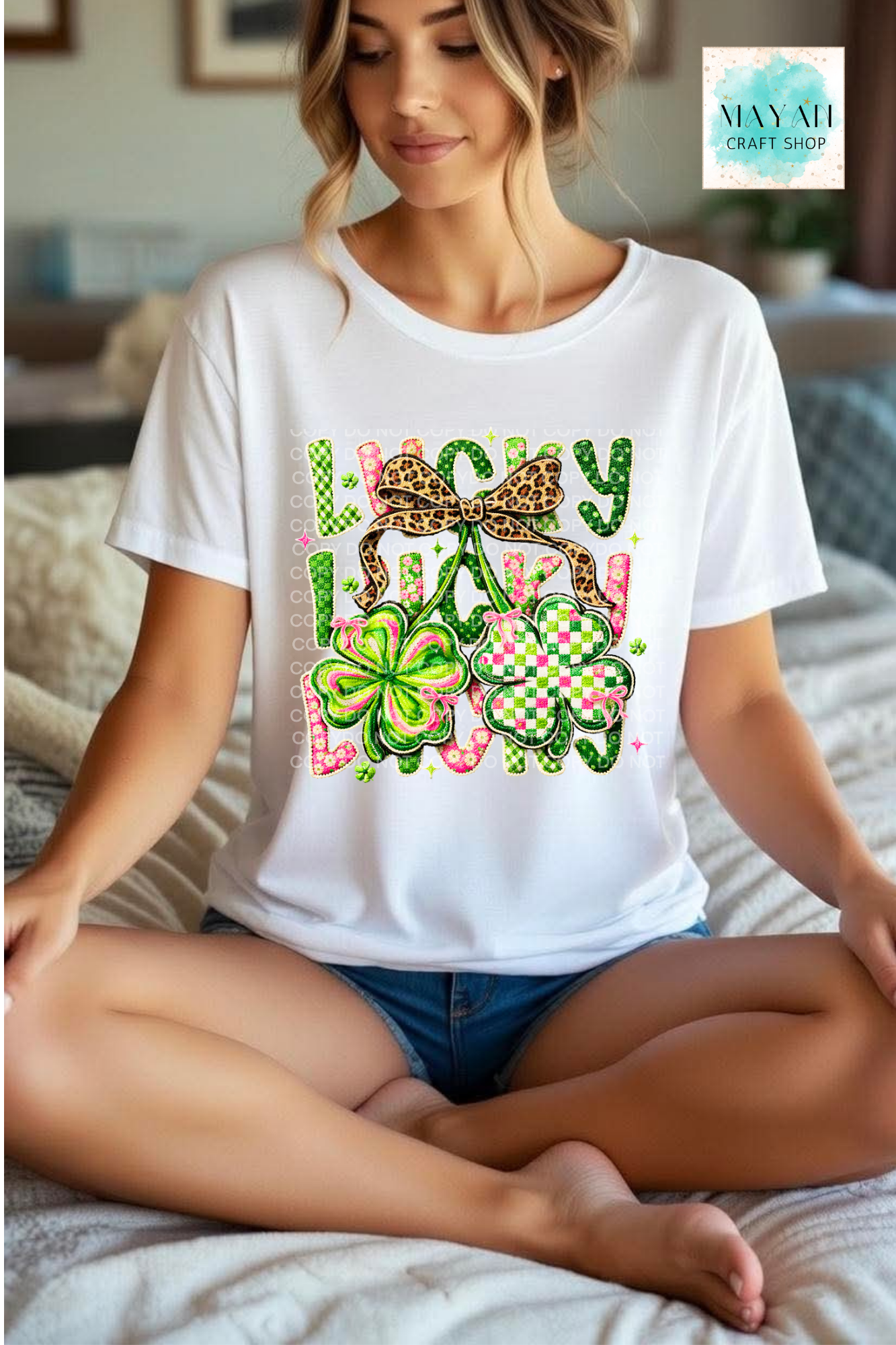 Woman wearing a white t-shirt with colorful graphics and text, sitting on a bed.